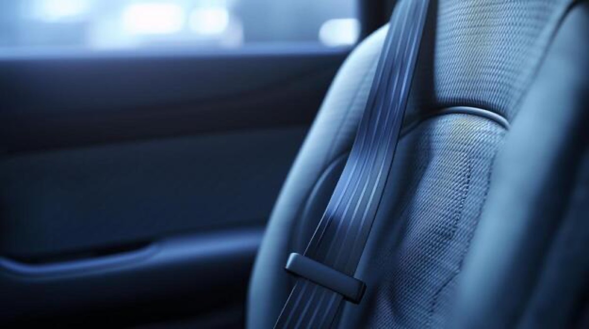 A seat belt lying across the shoulder of a car seat, photographed in cool daylight through the side window.