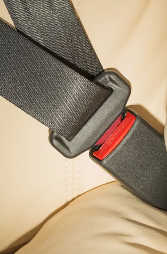 A dark seat belt with a red buckle release, fastened across a cream-coloured vehicle seat.