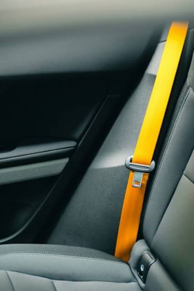 A bright yellow seat belt running diagonally across the grey interior trim of a car, seen from the rear seat.