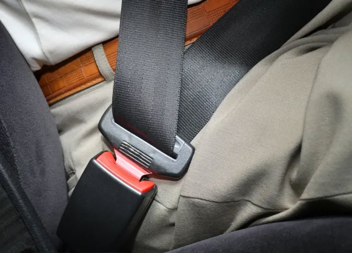 A fastened black seat belt with a red release button, shown across the lap of a seated occupant in a vehicle.