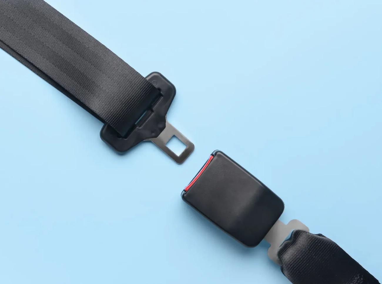 A complete seat belt assembly laid flat on a pale blue surface — black webbing, metal tongue and buckle receiver arranged side by side.