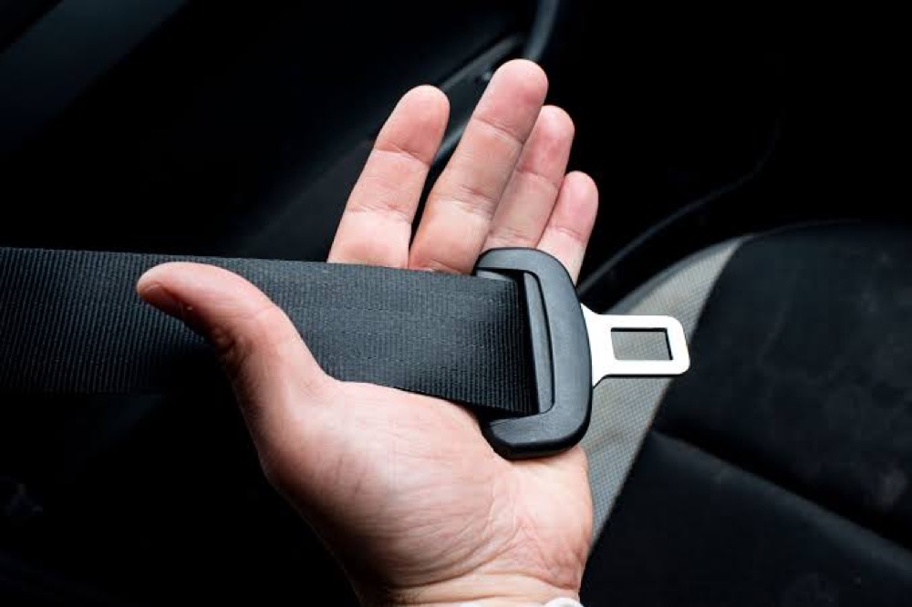 An open palm holding a black seat belt webbing strap and its metal tongue.